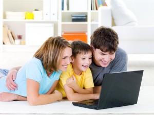 High-angle portrait of happy laughing young family with son lying on the floor with laptop